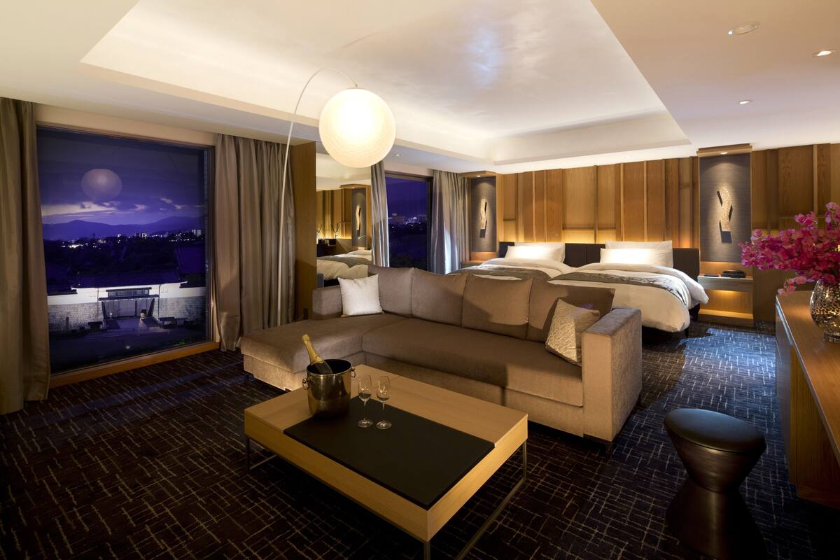 A modern hotel room with a large bed, a sofa, a coffee table, and a view of the city at night.