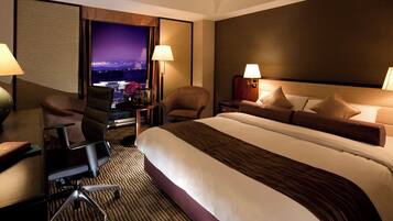 Ein Hotelzimmer mit einem großen Bett, zwei Sesseln, einem Schreibtisch mit Stuhl und Blick auf die Stadt.
