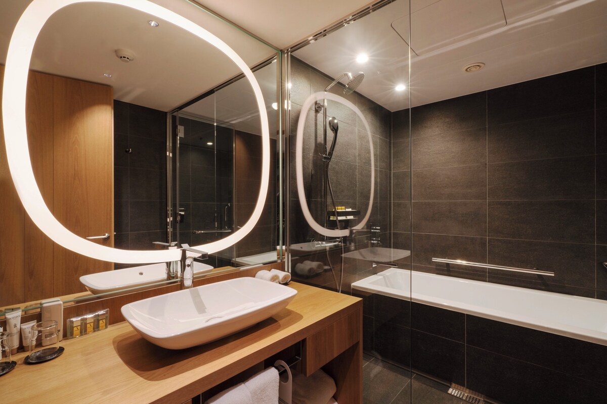 Une salle de bain moderne dotée d’un grand miroir, de deux vasques, d’une baignoire et d’une cabine de douche en verre.