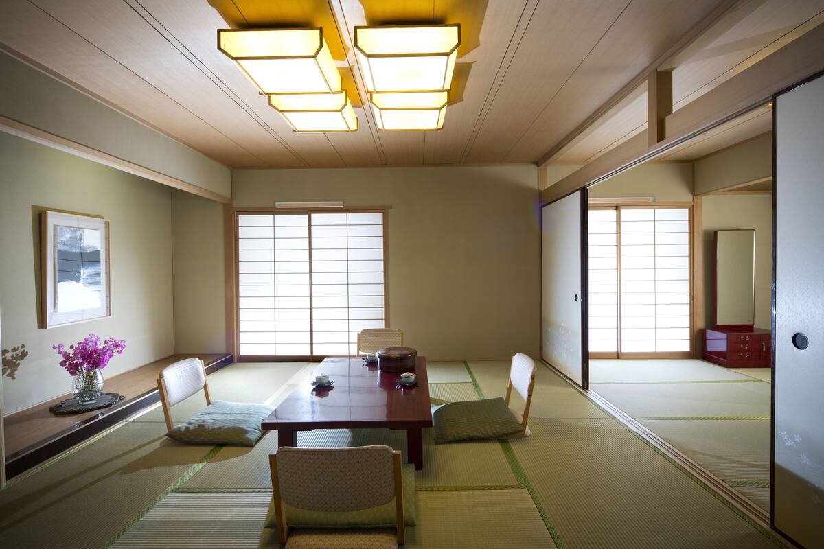 A traditional Japanese room with tatami flooring, a low table, chairs, and sliding doors.