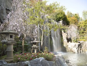 Un jardin paisible avec une cascade, des lanternes en pierre et des fleurs en pleine floraison.