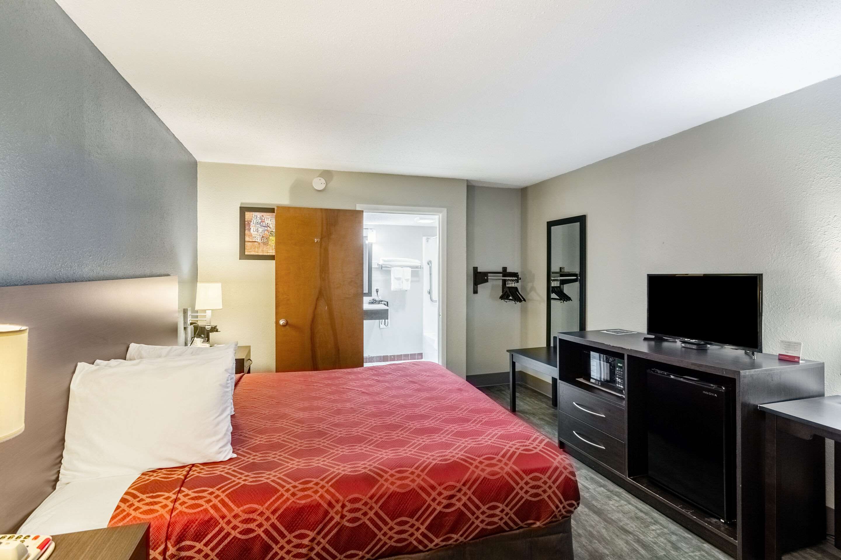 Una habitación de hotel con cama, televisor, escritorio y puerta que da a un baño.
