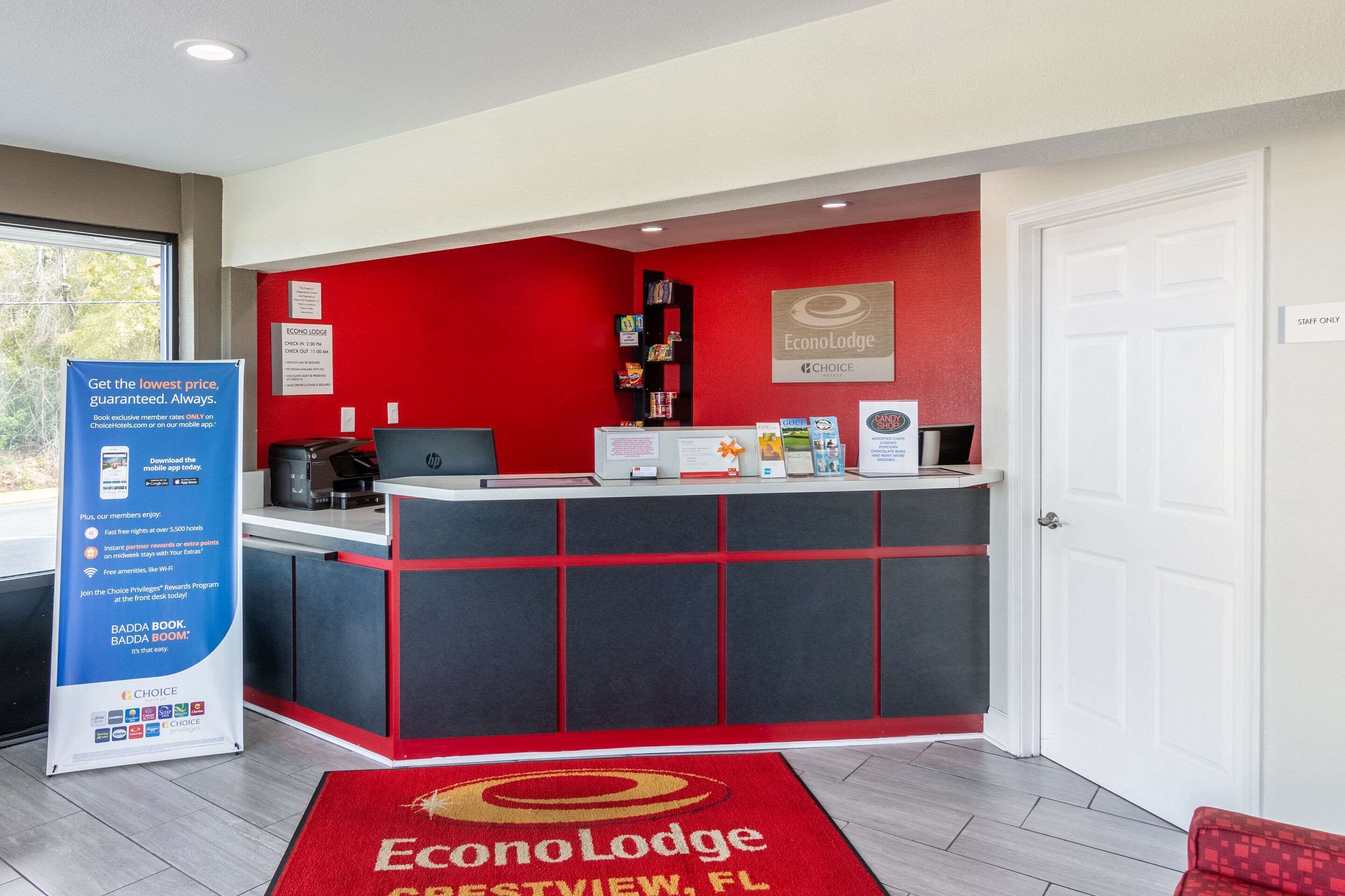 Un espace d’accueil avec un comptoir rouge et noir, une enseigne indiquant « EconoLodge », et un tapis rouge orné du nom de l’hôtel.