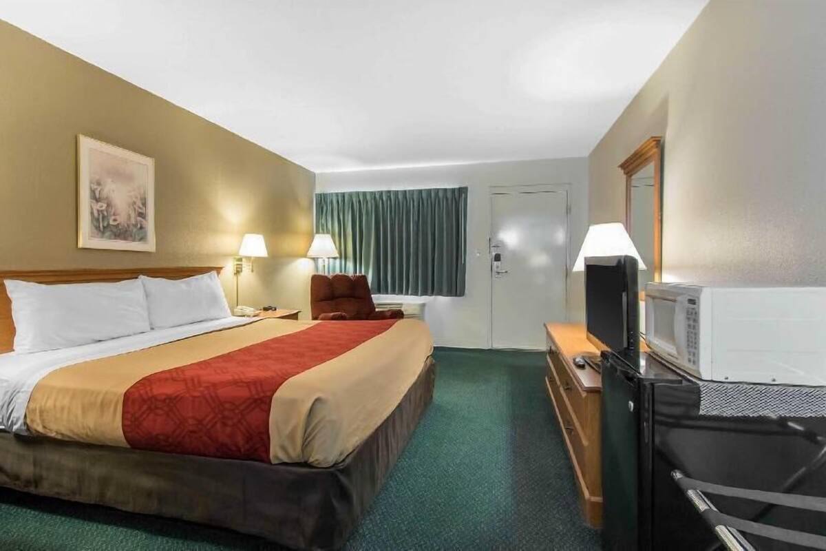 Habitación de hotel con cama, dos lámparas de noche, televisor, cómoda y una puerta.