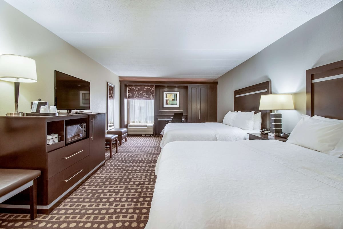 Quarto de hotel com duas camas, uma mesa, uma cadeira, uma televisão e casa de banho.