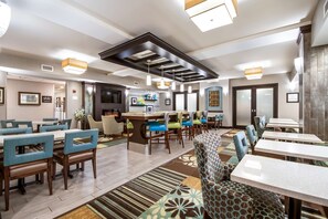 A modern hotel lobby with a central bar area, multiple seating arrangements, and a well-lit ceiling design.