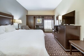 A hotel room with a large bed, a desk, a chair, a TV, and a wardrobe.