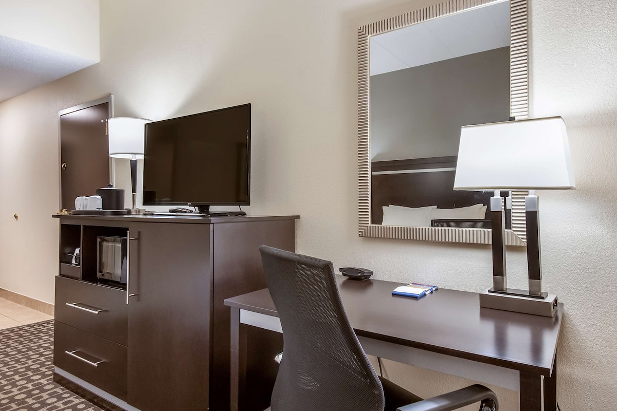 Quarto de hotel com escrivaninha, cadeira, televisão e espelho.