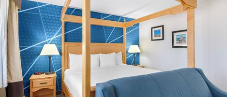 A four-poster bed with white linens, two bedside tables with lamps, a blue sofa, and a blue patterned wall.