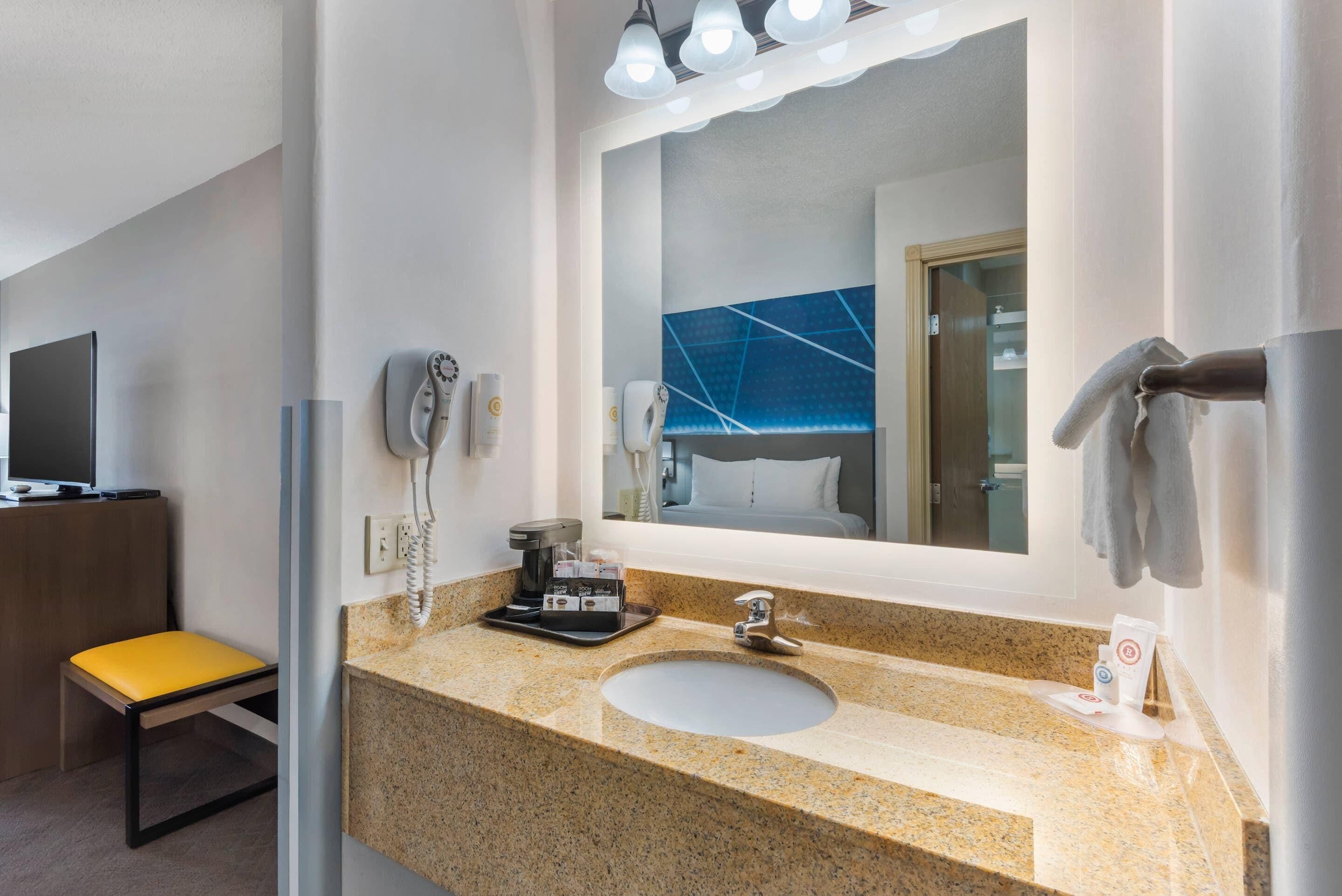 A hotel bathroom with a granite countertop, a sink, a mirror, a towel rack, a hairdryer, and a telephone.