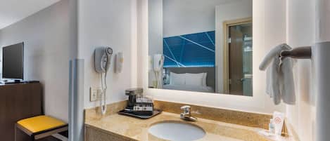 A hotel bathroom with a granite countertop, a sink, a mirror, a towel rack, a hairdryer, and a telephone.