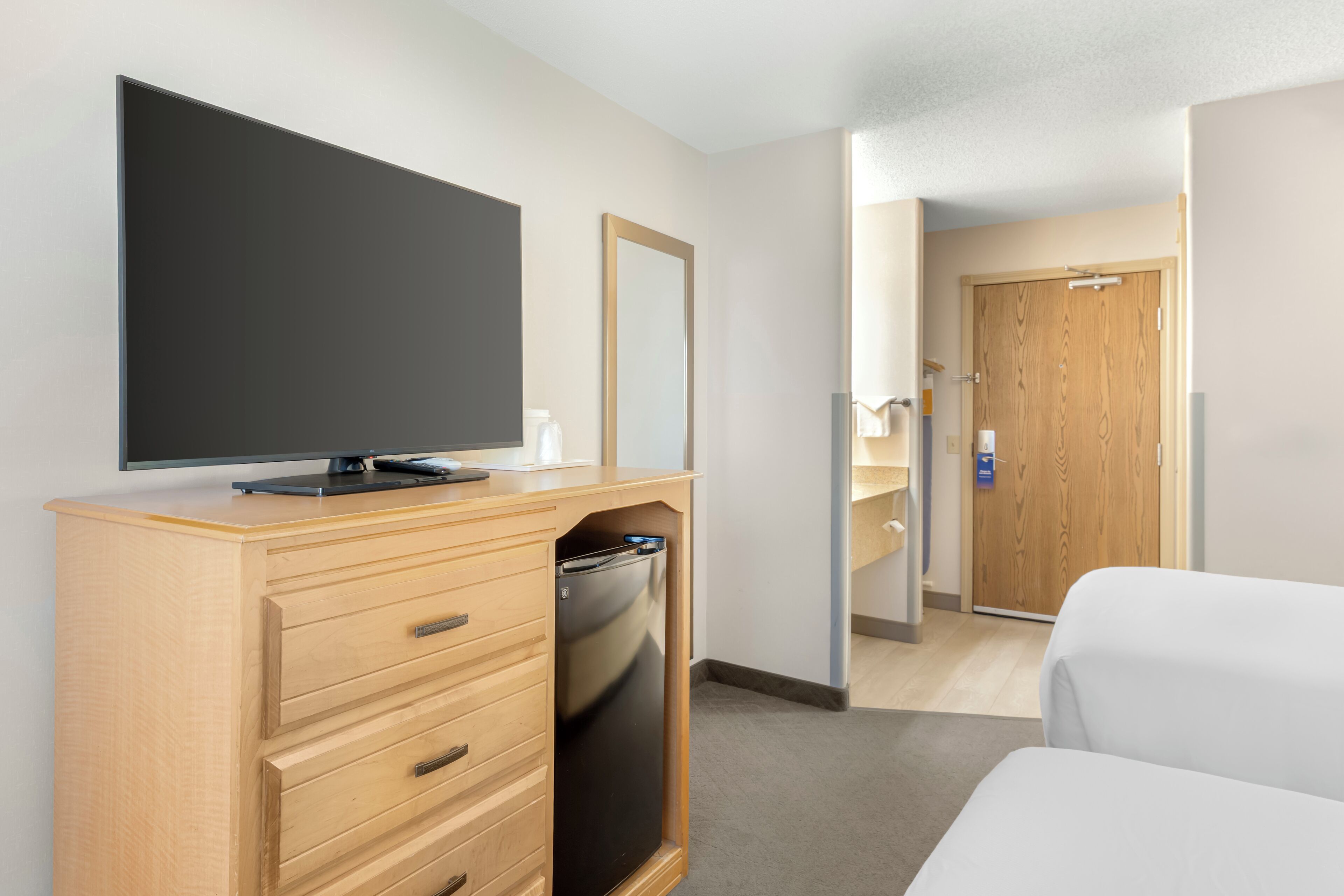 A hotel room with a wooden dresser, a television, a mirror, a door, and a bed.