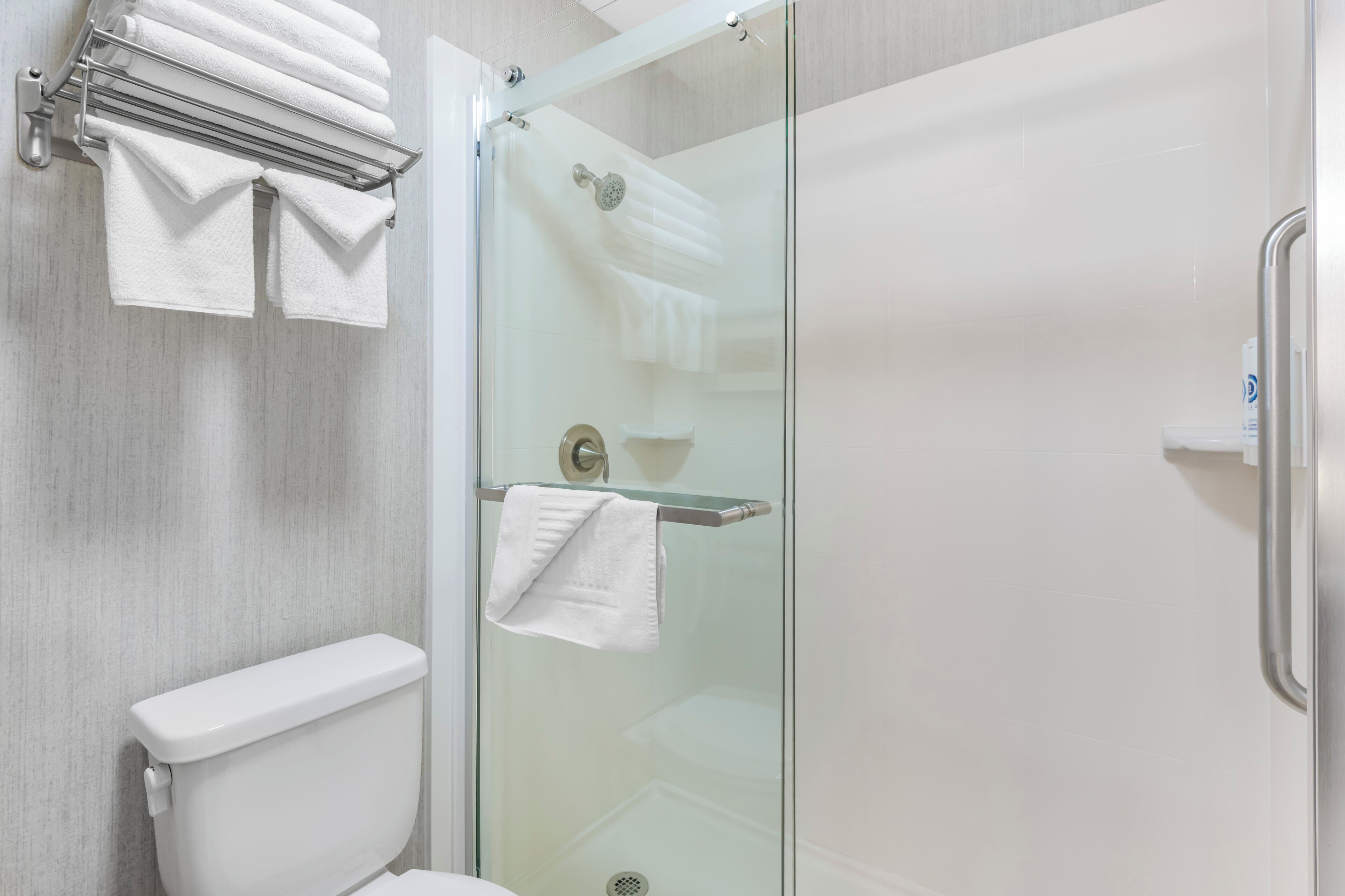 A modern bathroom with a glass shower enclosure, a toilet, and a towel rack with multiple towels.