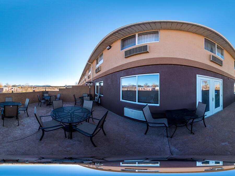 A building with a curved facade, outdoor seating area with tables and chairs, and a clear sky.