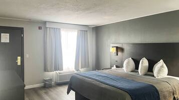 A hotel room with a bed, a nightstand, a wall-mounted lamp, and a window with curtains.