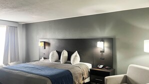 A hotel room with a large bed, a nightstand with a phone, a chair, and a wall-mounted light fixture. - Motel 6 – Chillicothe, MO (Chillicothe)