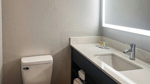 A bathroom with a white toilet, a sink with a mirror, and toiletries on the counter. - Motel 6 – Chillicothe, MO (Chillicothe)
