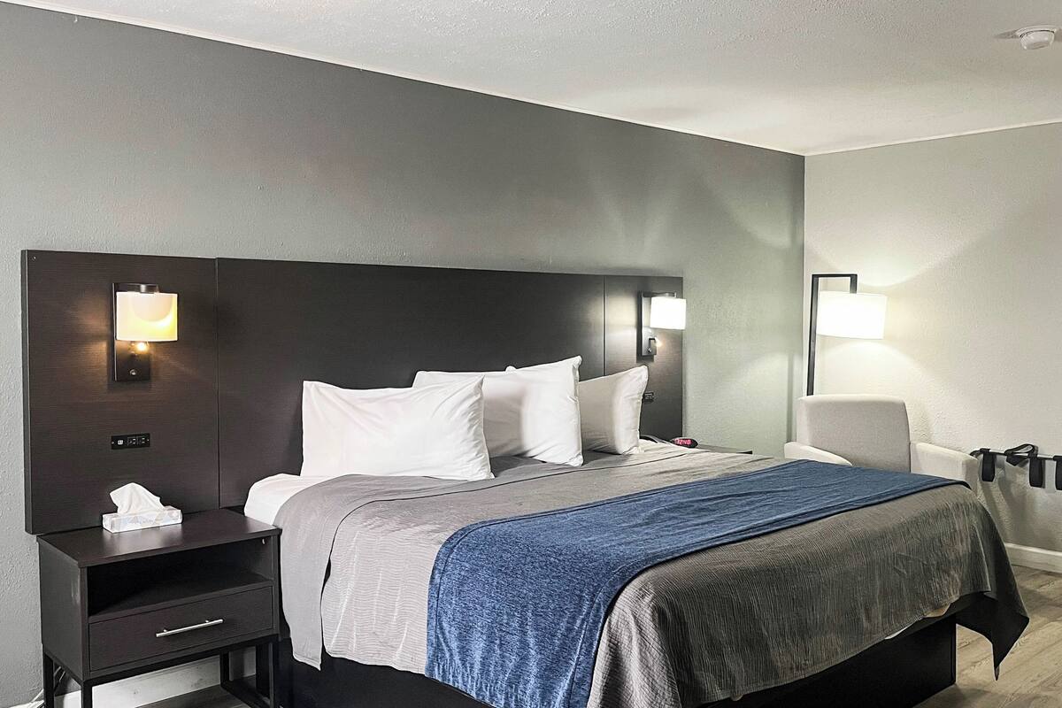 A hotel room with a bed, bedside tables, a chair, and wall-mounted lamps.