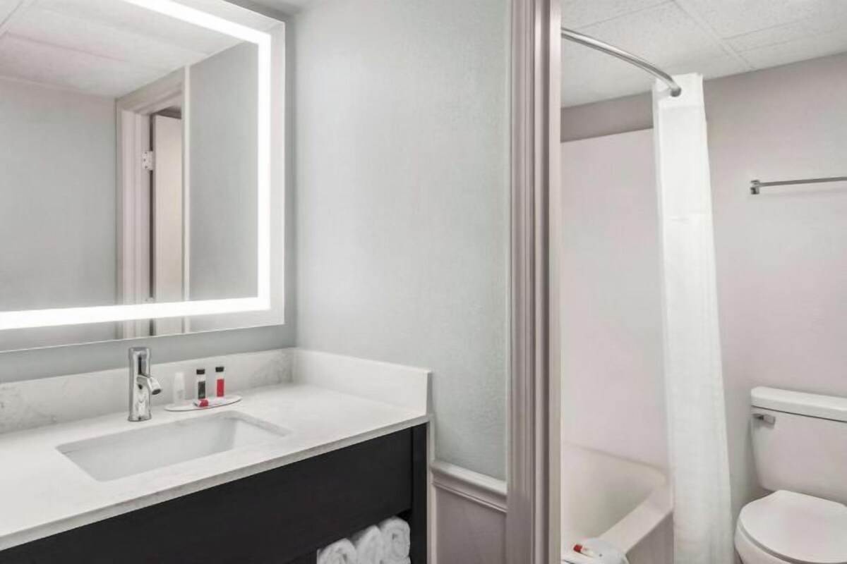 A modern bathroom with a large mirror, a sink, a shower, and a toilet.