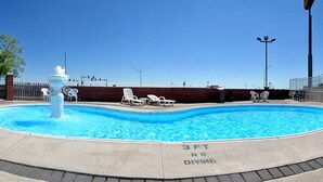 A swimming pool with a fountain, surrounded by lounge chairs and a brick wall. - Motel 6 – Chillicothe, MO (Chillicothe)