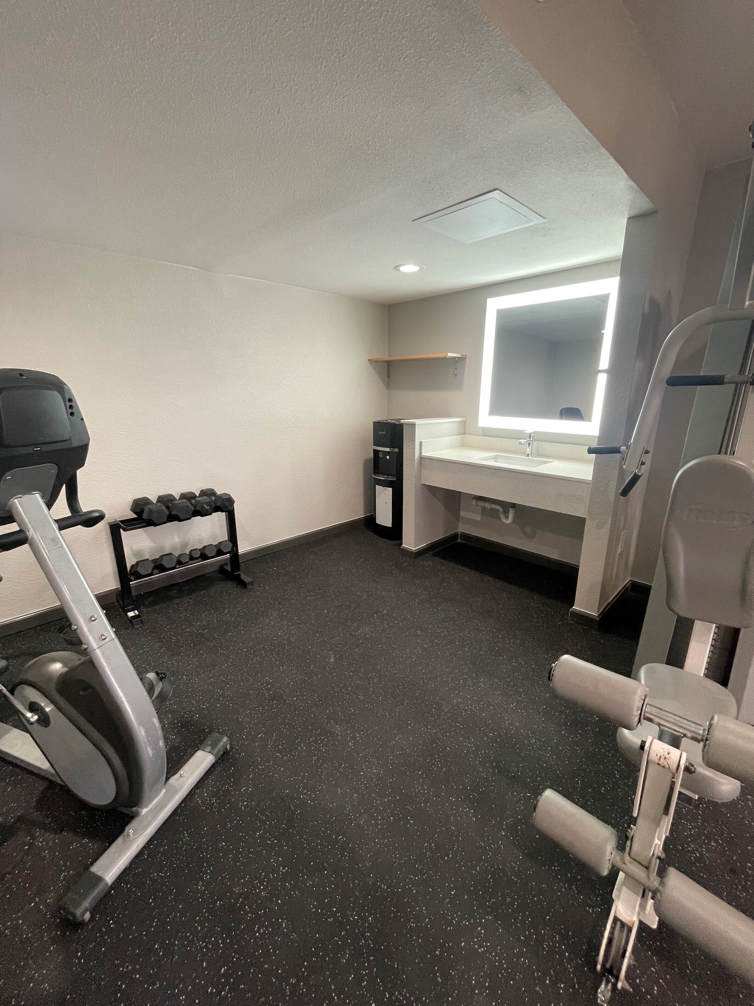 A gym with exercise equipment, a mirror, and a small shelf.