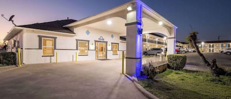 A hotel with a covered entrance, a signboard, and a parking area.