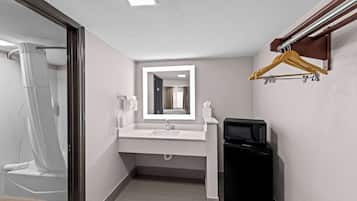 A modern bathroom with a white sink, a mirror, a black microwave, and a wooden hanger rack.