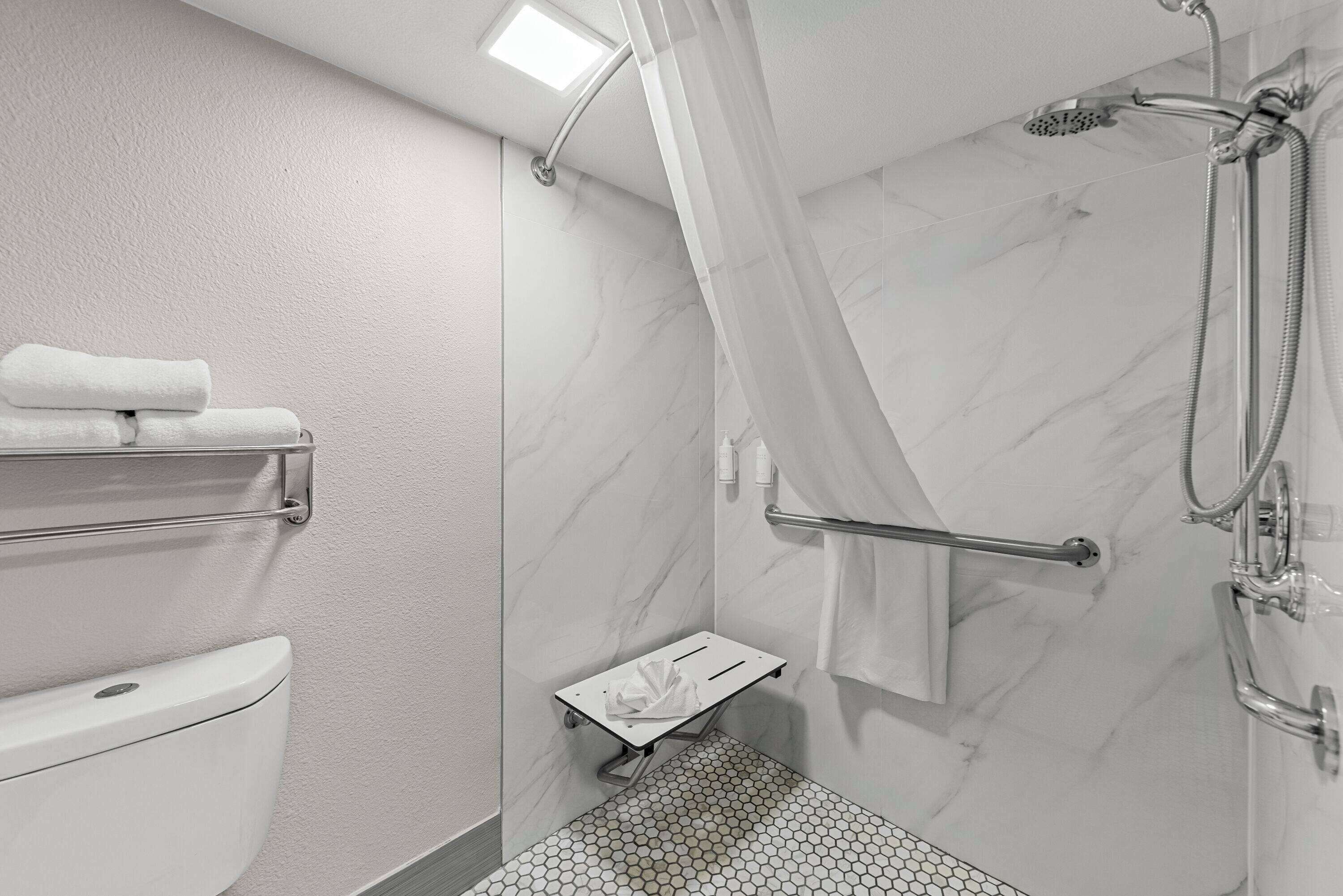 A bathroom with a toilet, a shower with a glass door, a towel rack, and a small shelf.