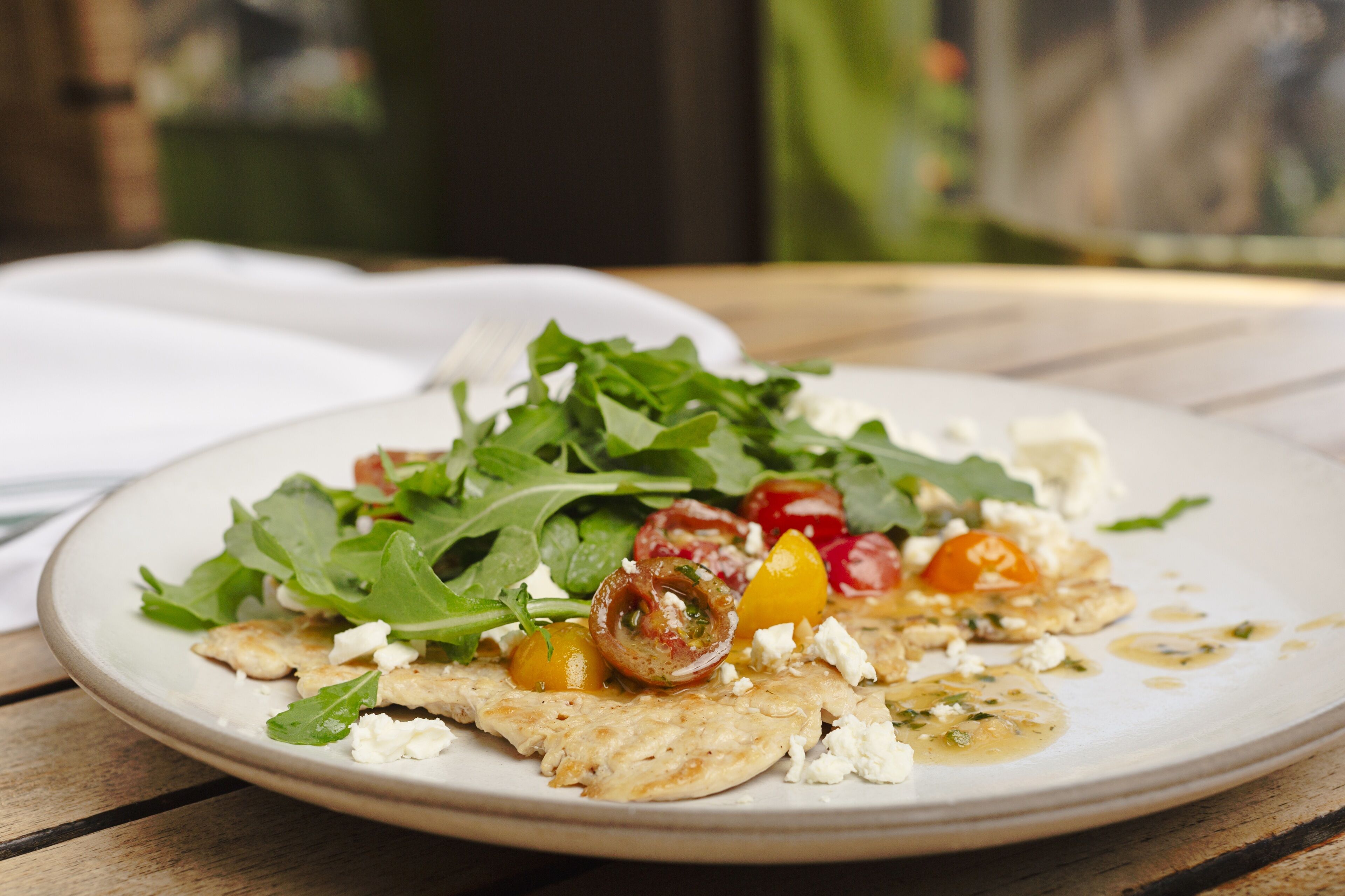A plate of food with greens, tomatoes, and cheese on a wooden table.