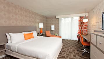 A hotel room with a large bed, a desk with a chair, a television, and a window with curtains.