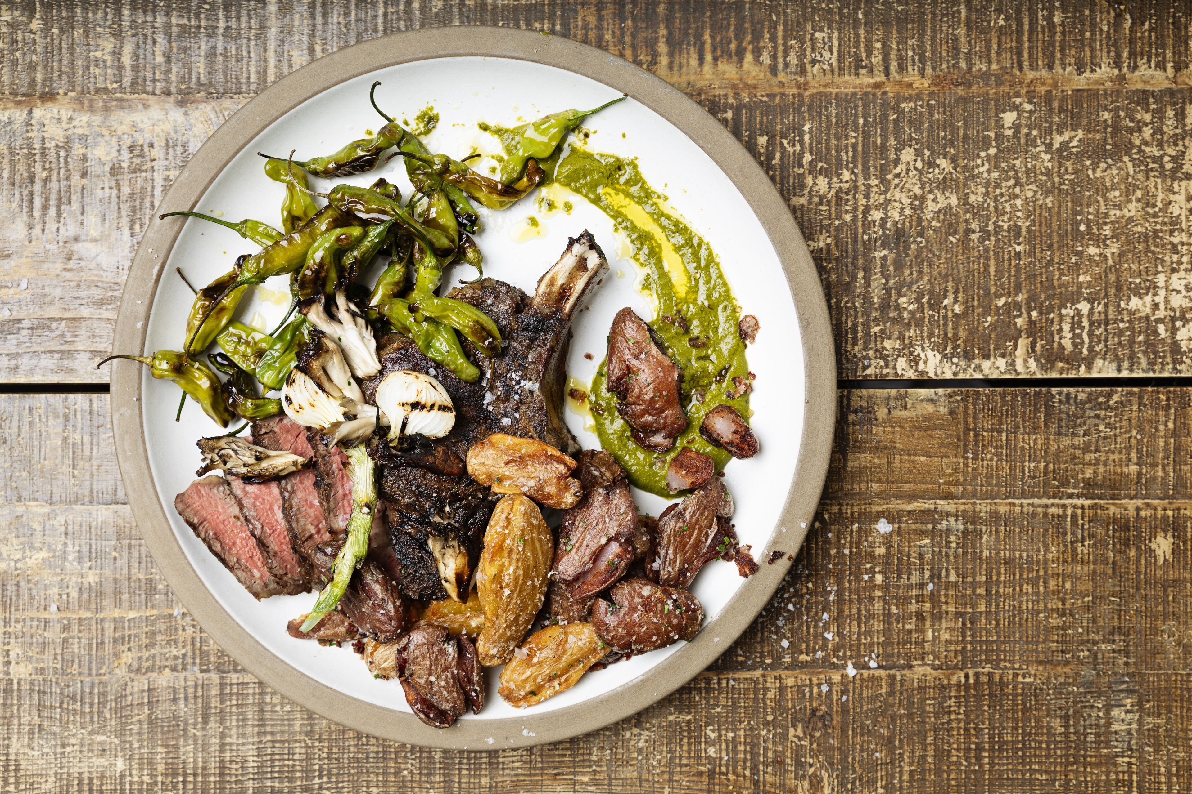 Un plato de comida con carne a la parrilla, verduras y salsa verde.