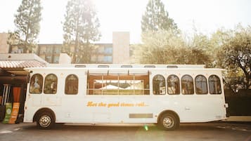 A white food truck with the text "Let the good times roll..." parked in front of a building with trees and a tiled roof.