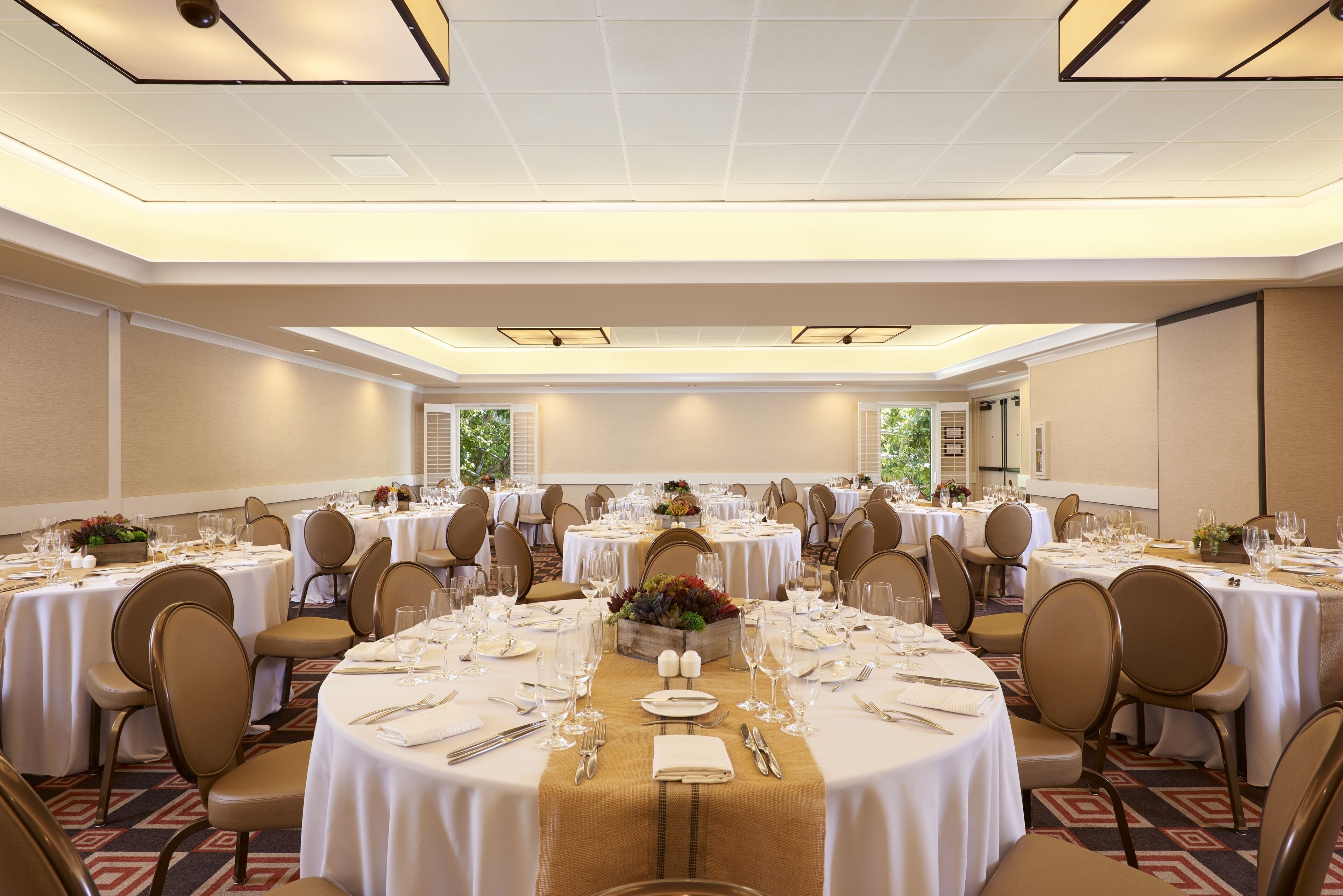 A banquet hall with round tables set for dining, equipped with chairs, tablecloths, and centerpieces.