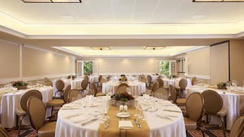 Un salón de banquetes con mesas redondas dispuestas para el servicio de comidas, equipado con sillas, manteles y centros de mesa.
