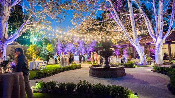 An outdoor garden area with a fountain, string lights, and trees. - The Garland (North Hollywood)