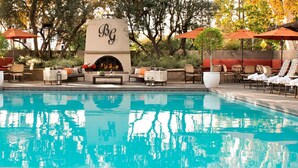 A pool area with a fireplace, outdoor seating, and umbrellas. - The Garland (North Hollywood)