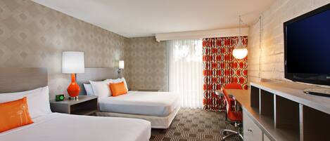 A hotel room with two beds, a desk, a television, and a patterned carpet.