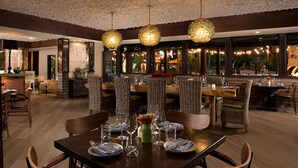 A restaurant with a high ceiling, wicker chairs, and a bar area.