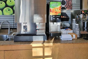 Eine gewerbliche Küche mit berührungsloser Wasserspender, einer Kaffeemaschine und einem Saftspender.