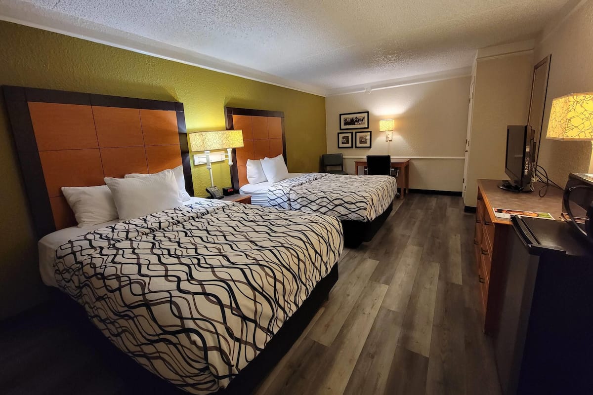 A hotel room with two beds, a desk, a chair, a TV, and a lamp.