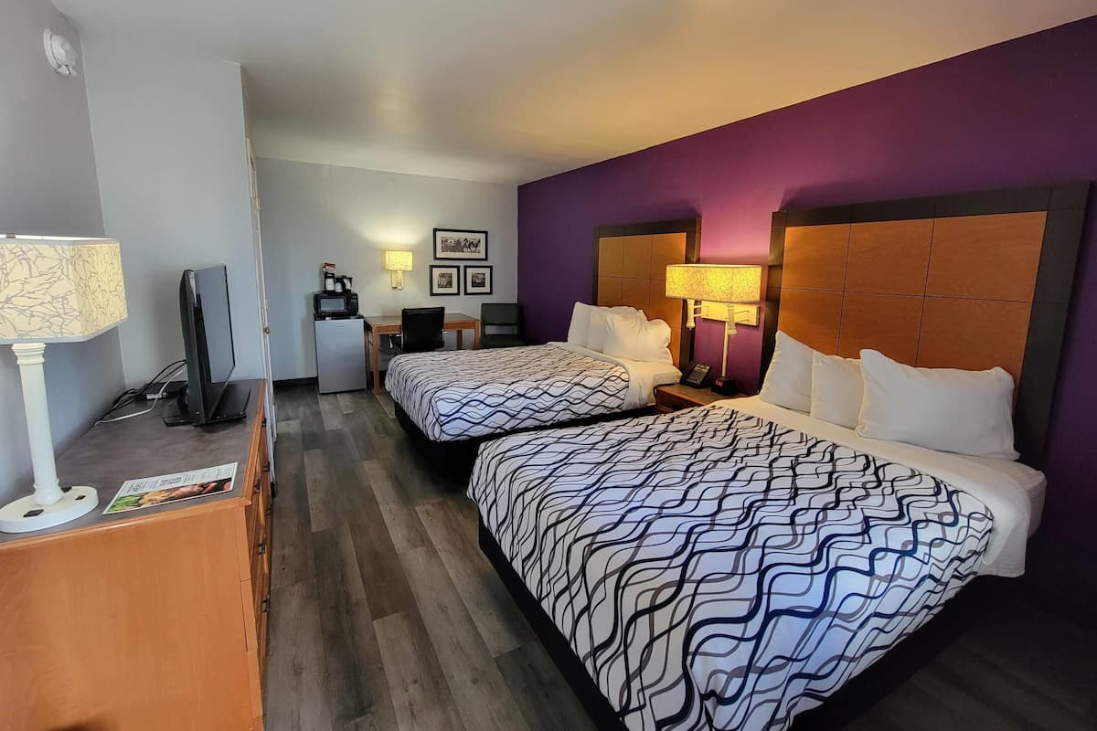 A hotel room with two beds, a desk, a television, and a coffee machine.