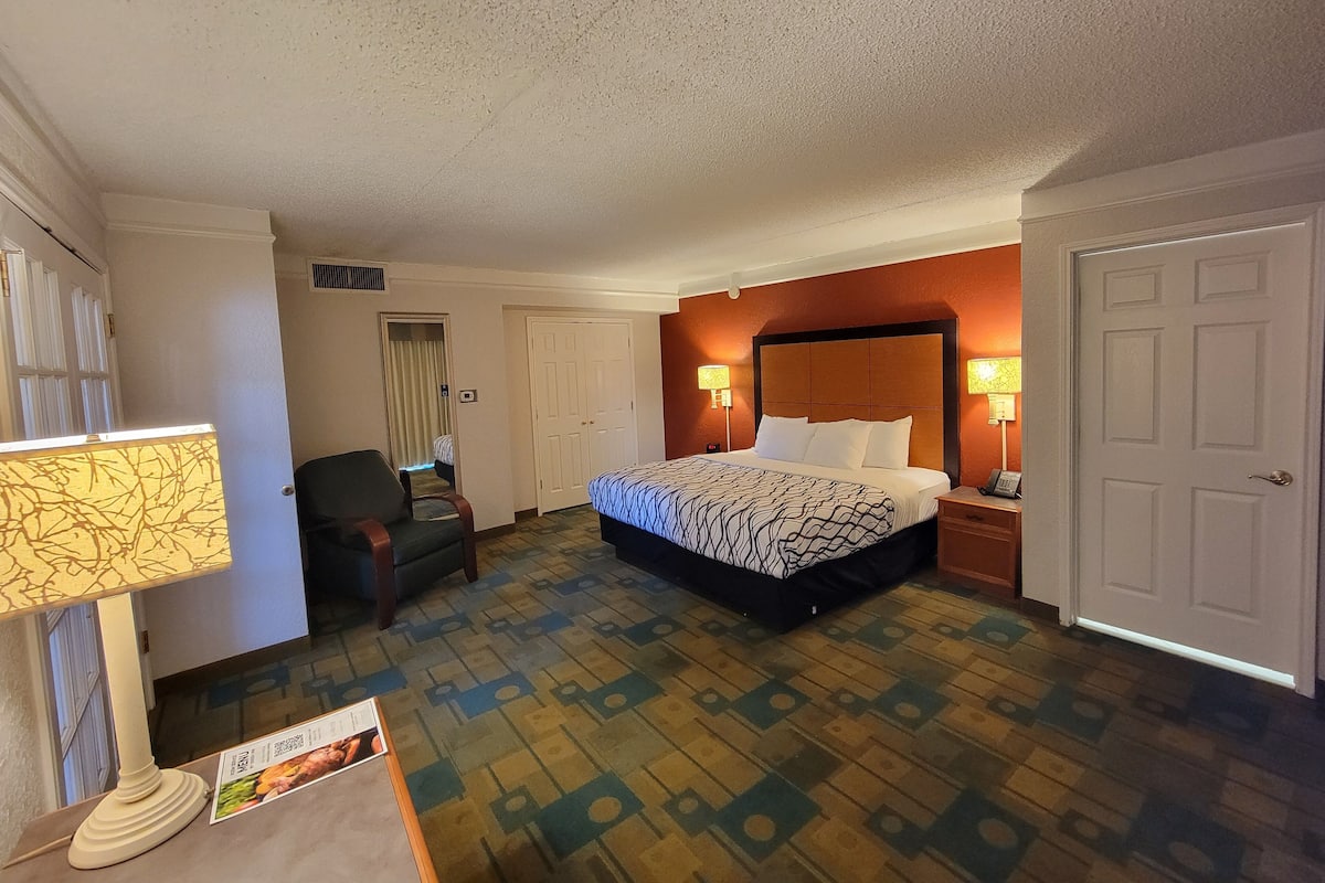 A hotel room with a bed, bedside table, lamp, chair, and a door.