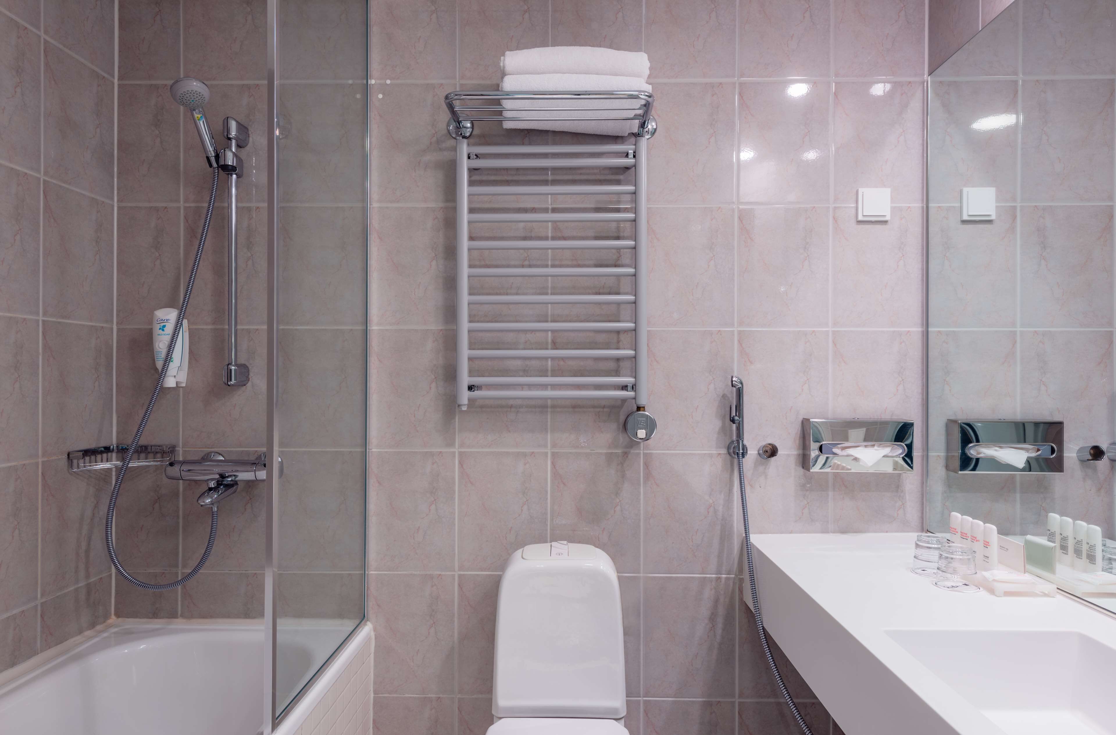 Un baño moderno con ducha envuelta en vidrio, inodoro blanco, perchero y tocador con artículos de aseo.