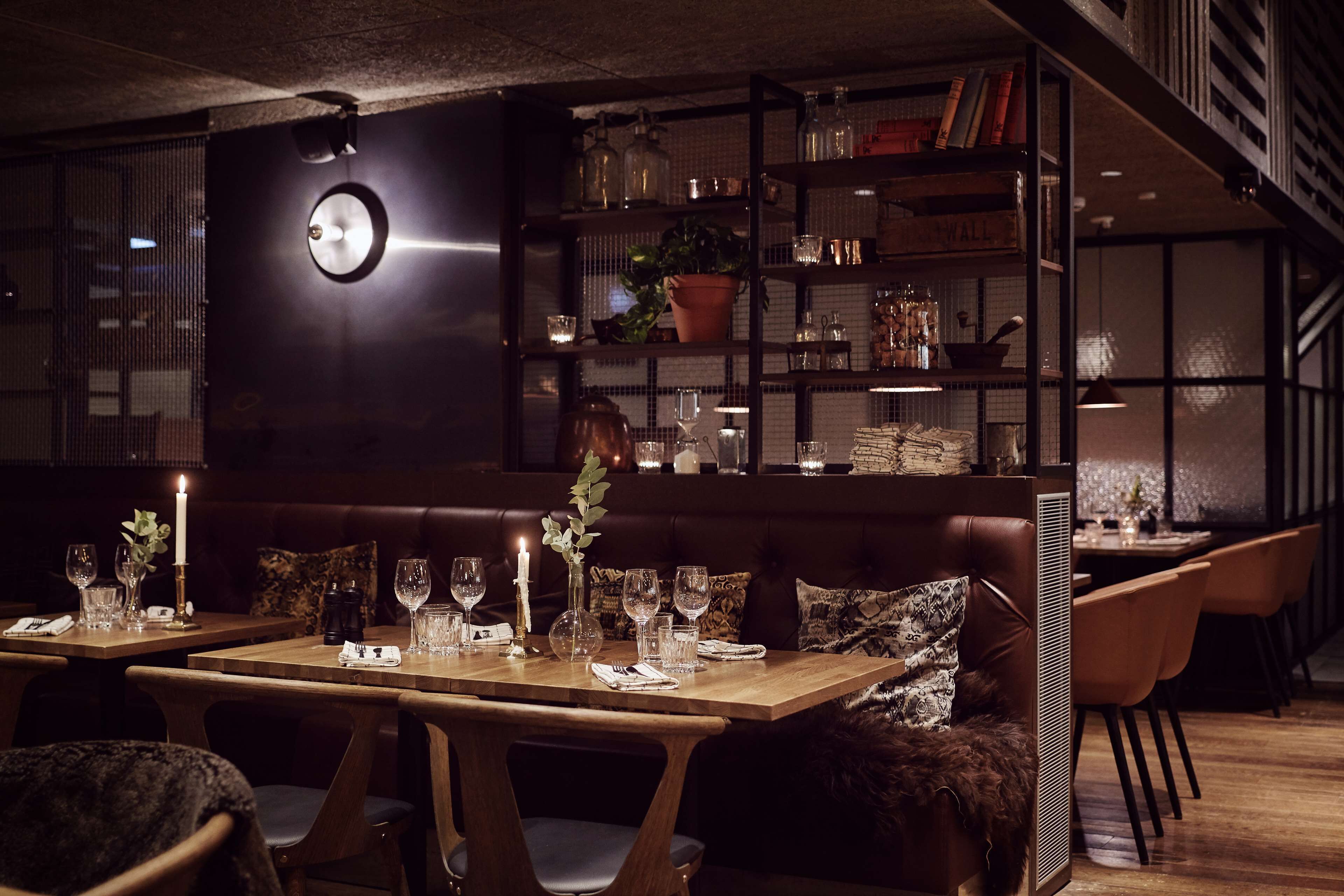 A dimly lit restaurant with wooden tables and chairs, a dark-colored sofa, and a bookshelf filled with books and decorative items.