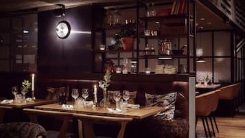 A dimly lit restaurant with wooden tables and chairs, a dark-colored sofa, and a bookshelf filled with books and decorative items.
