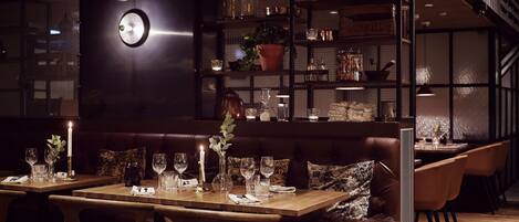 A dimly lit restaurant with wooden tables and chairs, a dark-colored sofa, and a bookshelf filled with books and decorative items.