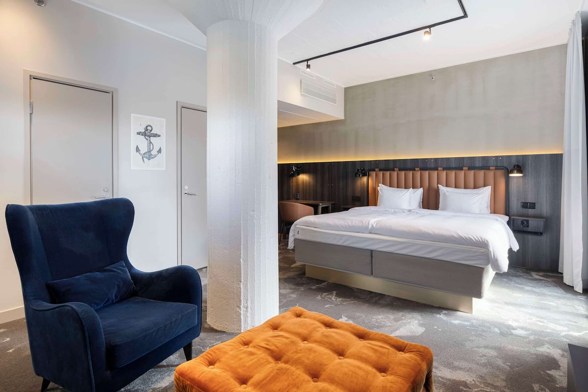 Moderni hotellihuone, jossa on suuri sänky, sininen nojatuoli ja oranssi rahi.