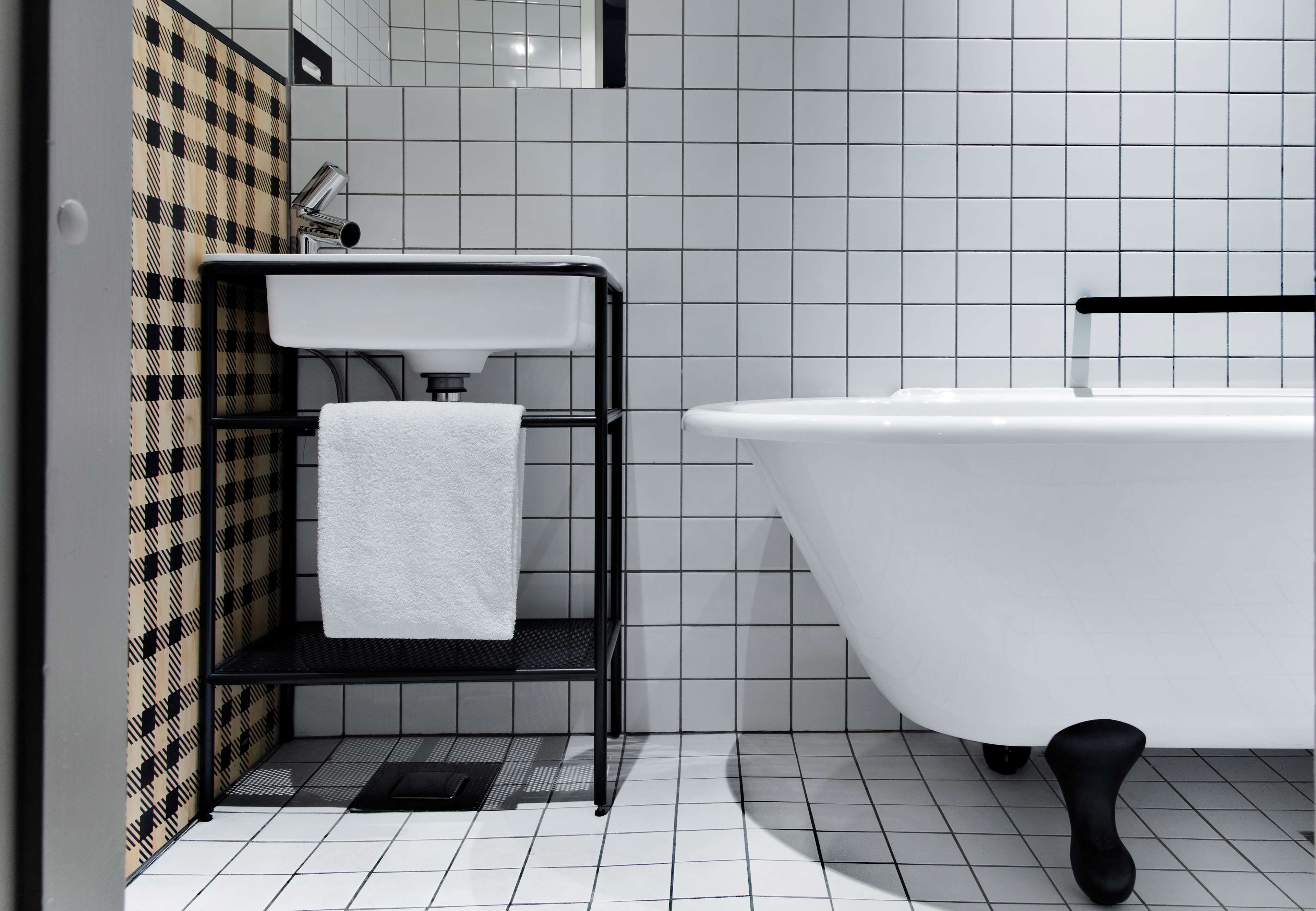 A bathroom with a white bathtub, a black metal shelf with a white towel, and a checkered wall pattern.