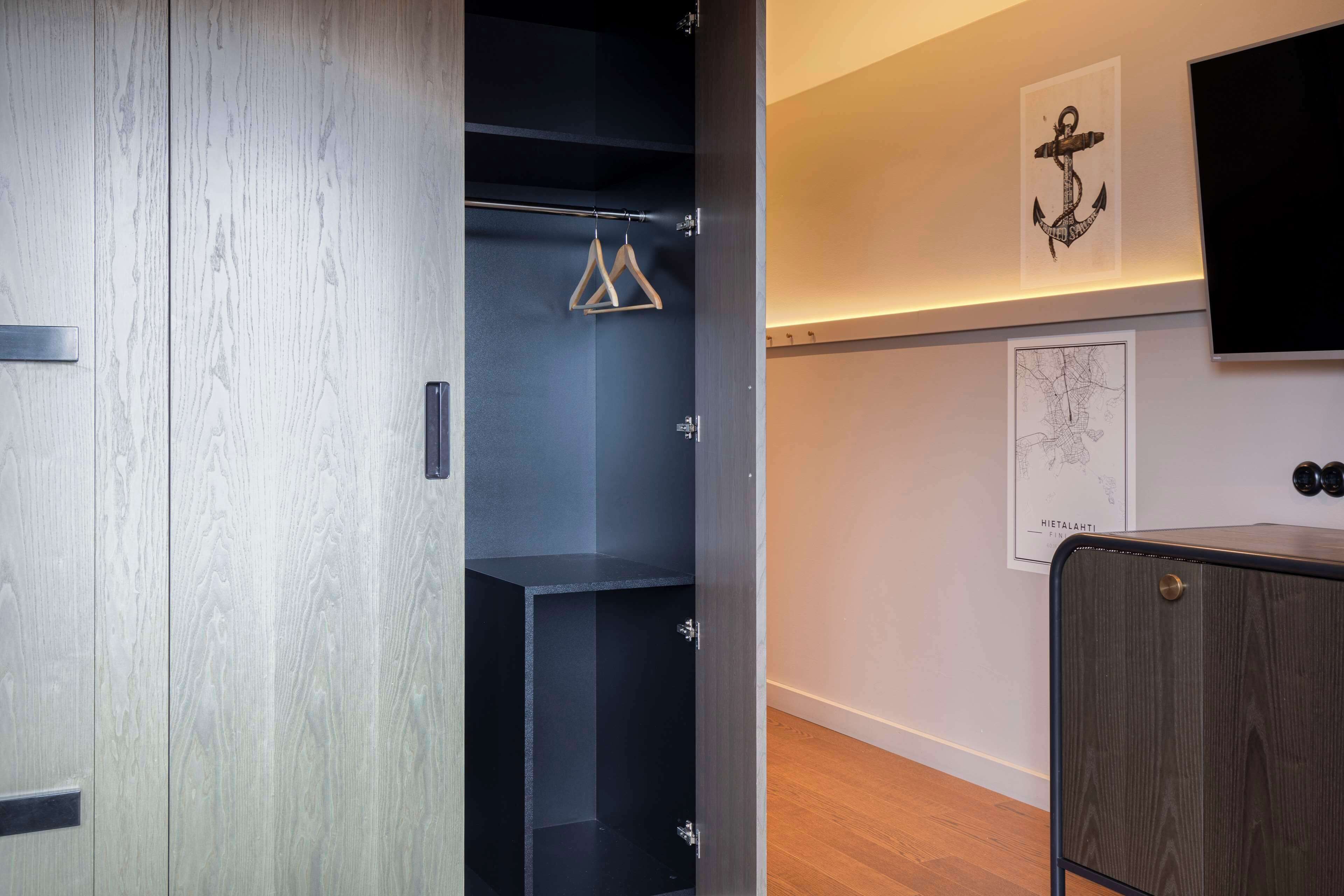 Une chambre moderne avec une armoire en bois, un portant noir et un téléviseur fixé au mur.