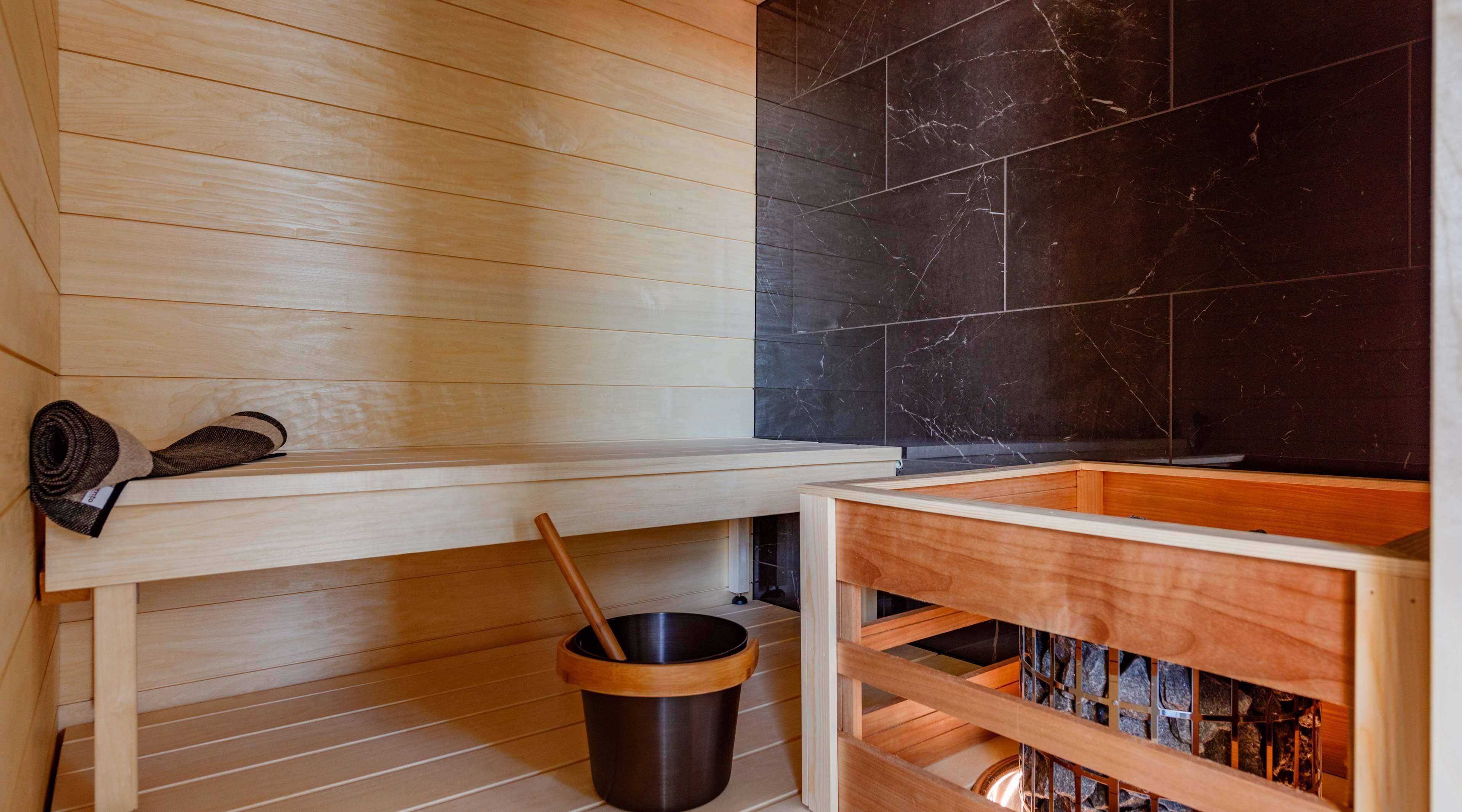 A sauna room with wooden benches, a black marble wall, and a wooden bucket.